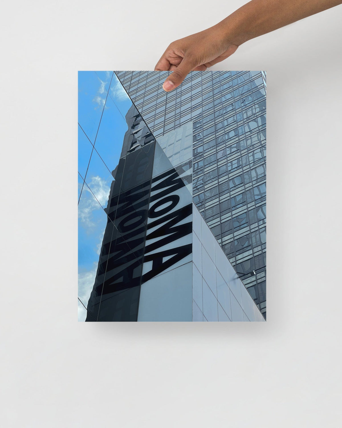 Hand holding a photo of a building with 'MOMA' branding against a blue sky.