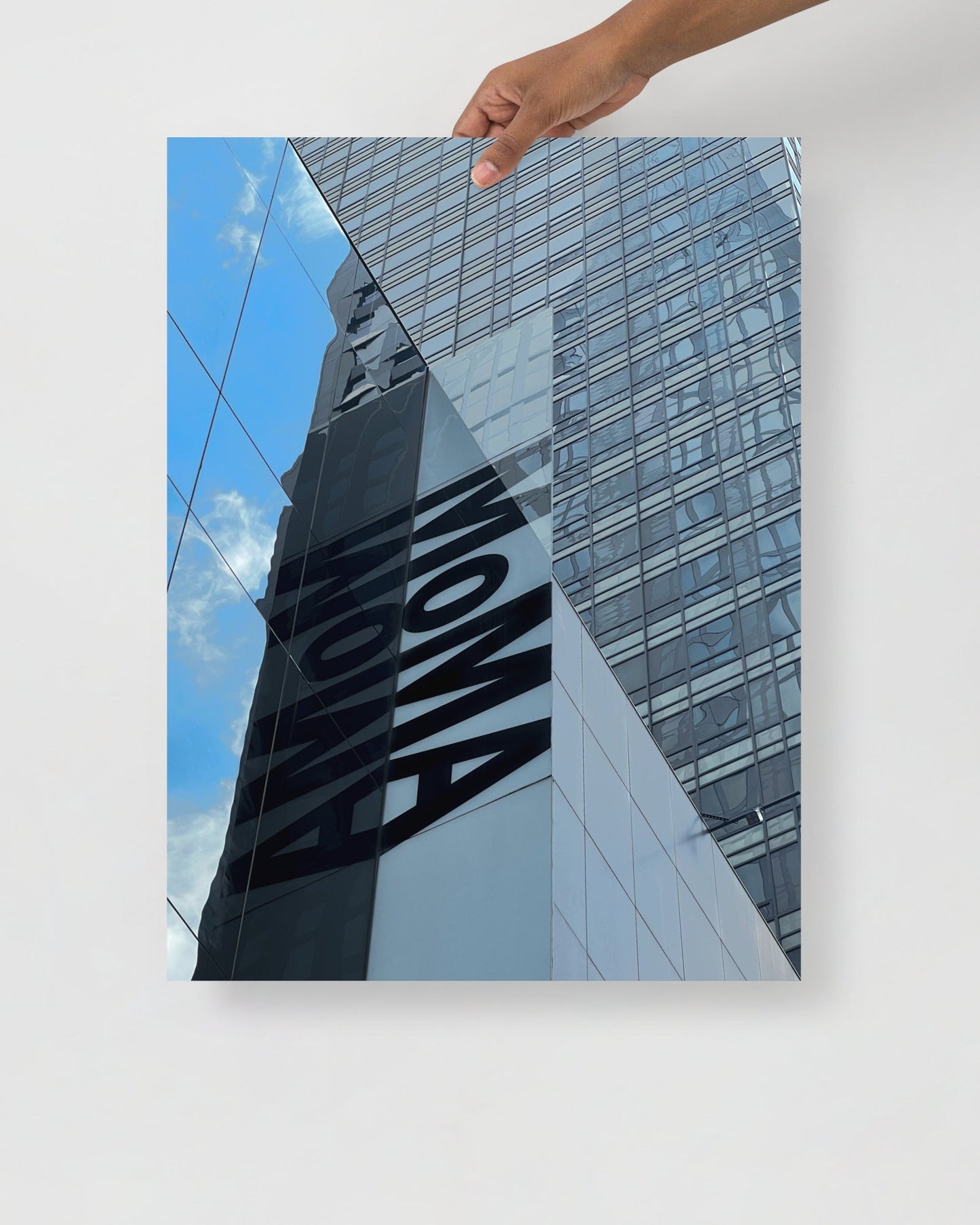 Hand holding a photo of a building with 'MOMA' branding against a blue sky.
