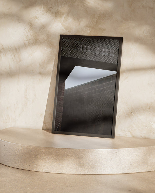 Black rectangular object on a beige pedestal against a textured wall.