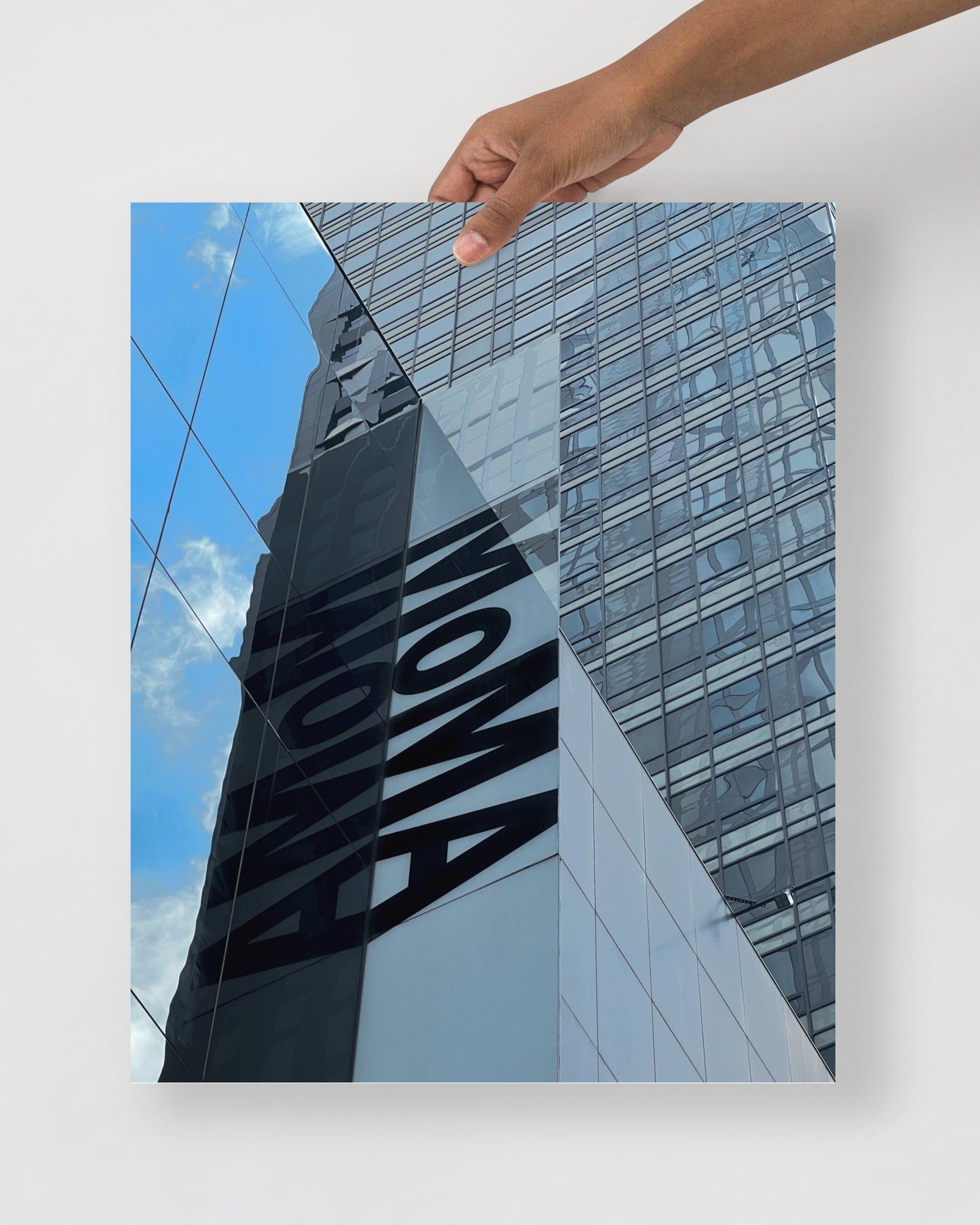 Hand holding a photo of a building with 'MOMA' branding against a blue sky.