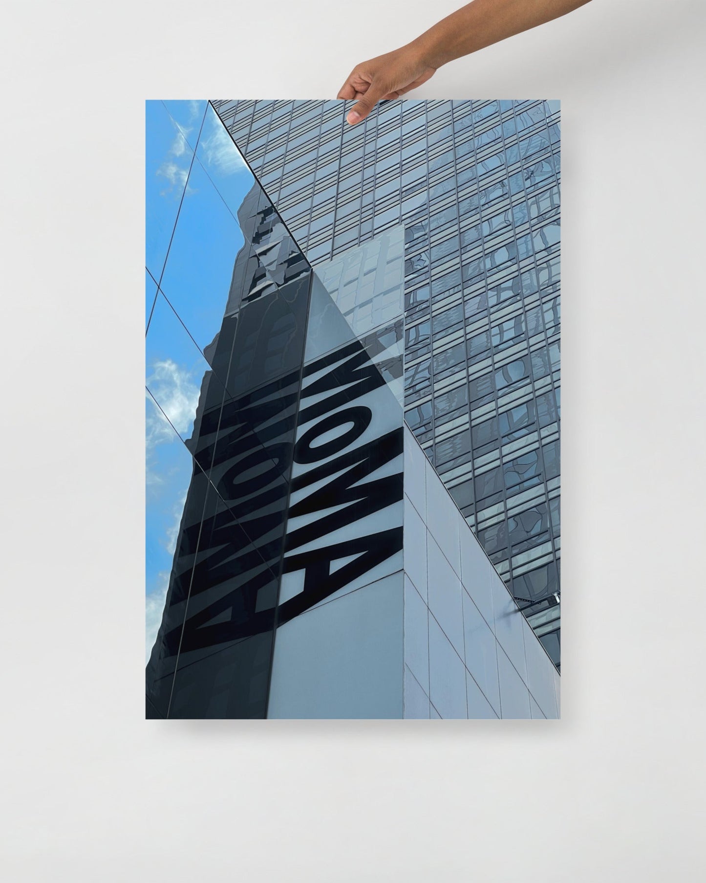 Hand holding a photo of a building with 'MOMA' branding against a blue sky.