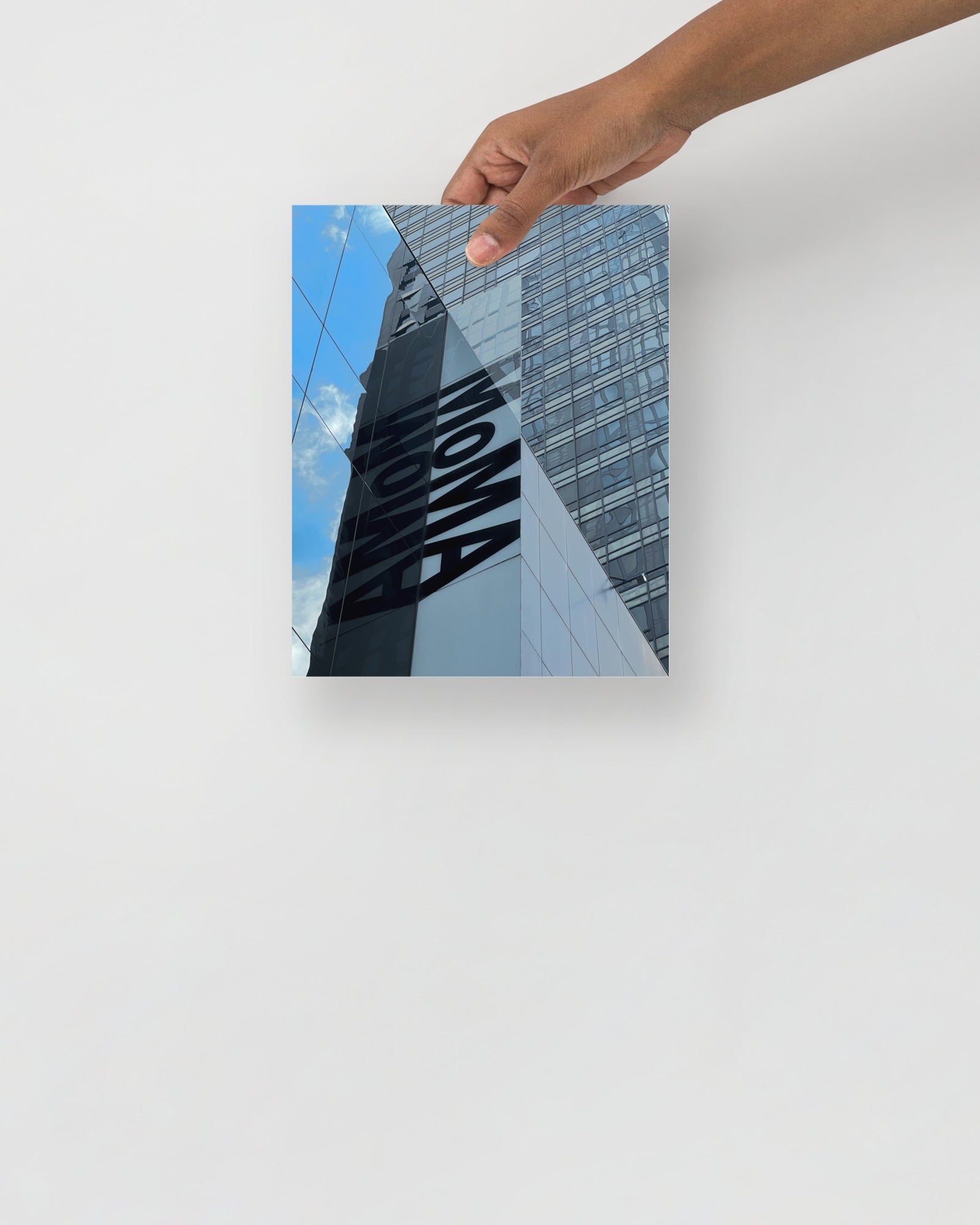Hand holding a photo of a building with 'MOMA' branding against a blue sky.